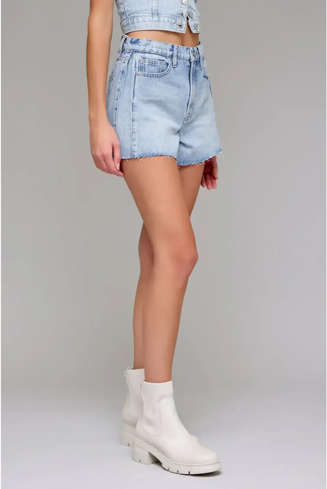 Person wearing light blue denim shorts and white boots on a gray background