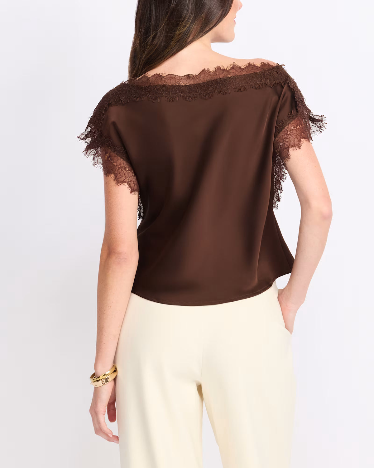 A woman shown from the back wearing a dark brown satin top with lace trim at the neckline and sleeves, paired with cream-colored pants, against a plain white studio background.