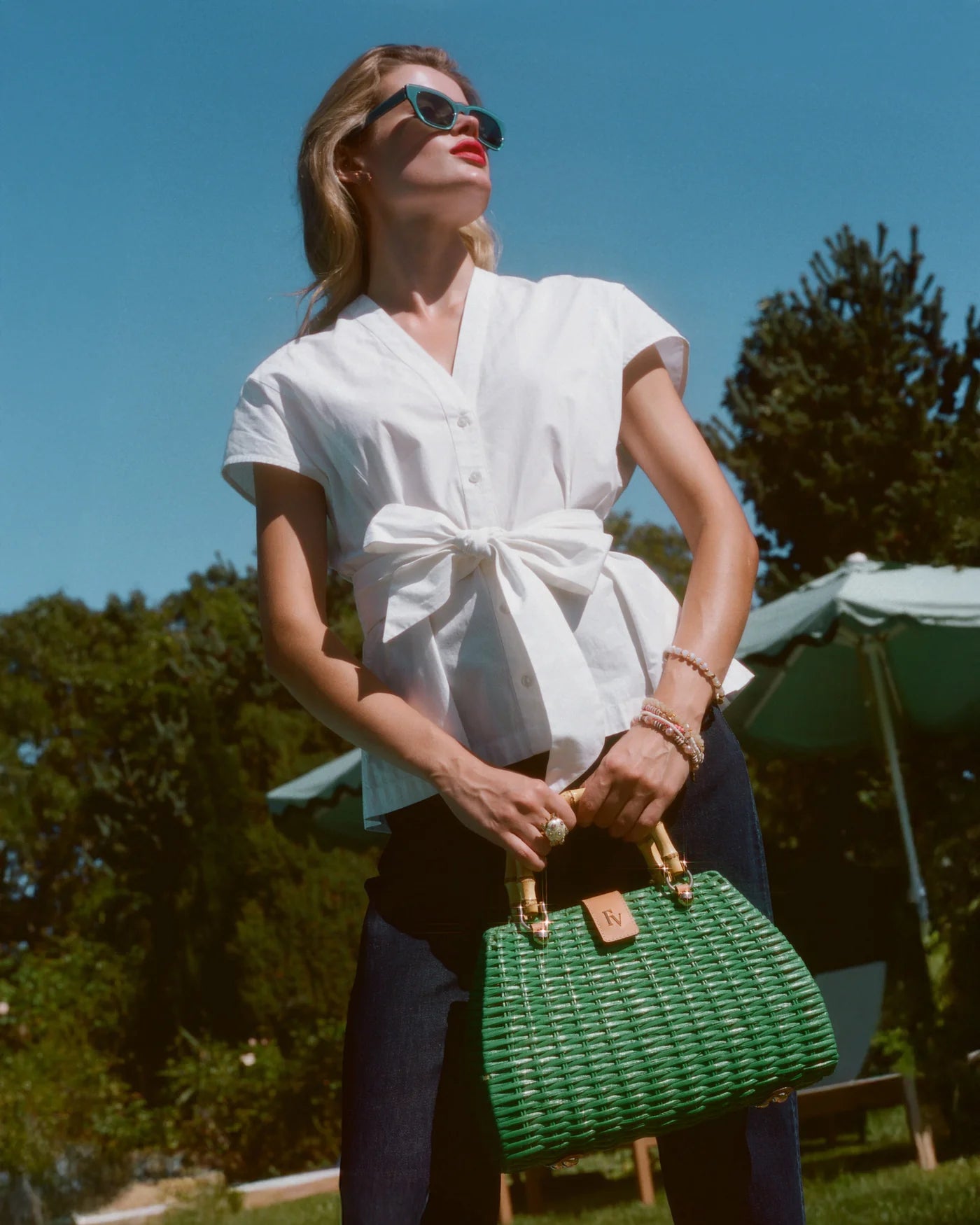 Woman in a white blouse and sunglasses holding a green handbag outdoors.