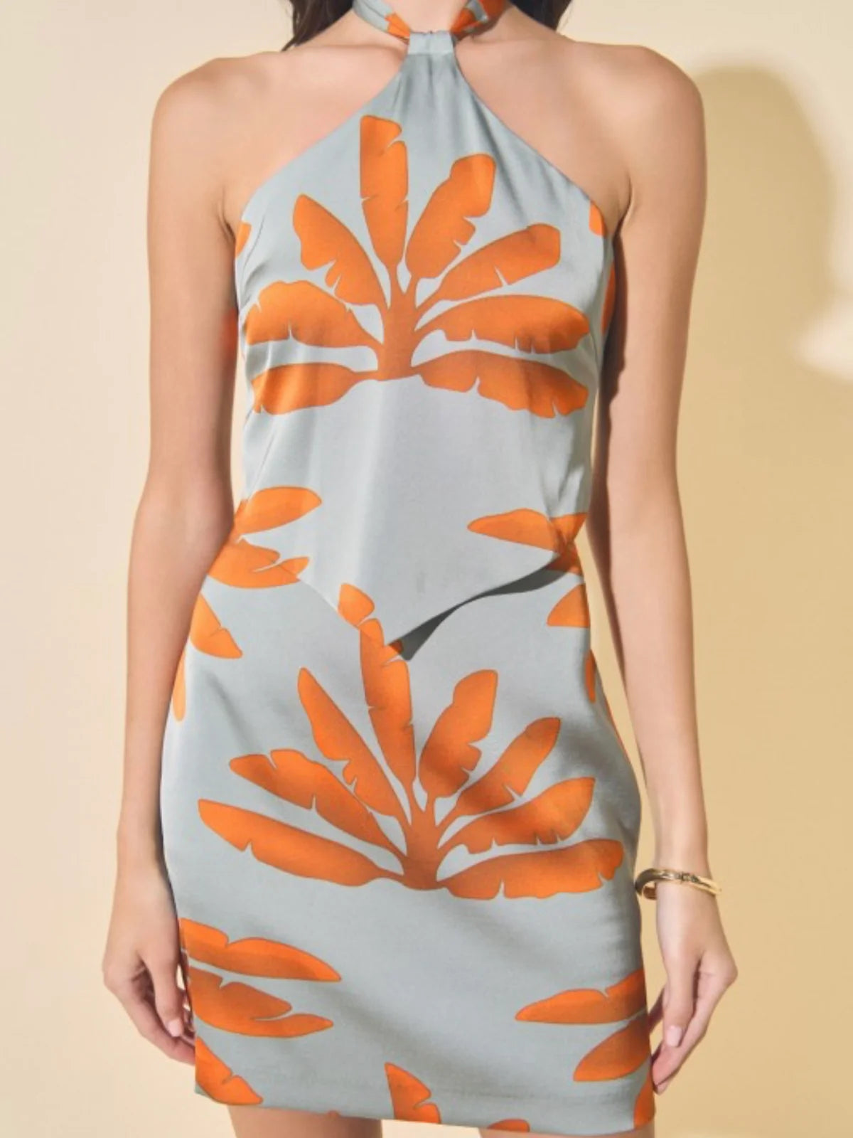 Woman wearing a halter neck dress with orange leaf pattern on a beige background