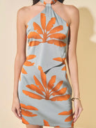 Woman wearing a halter neck dress with orange leaf pattern on a beige background