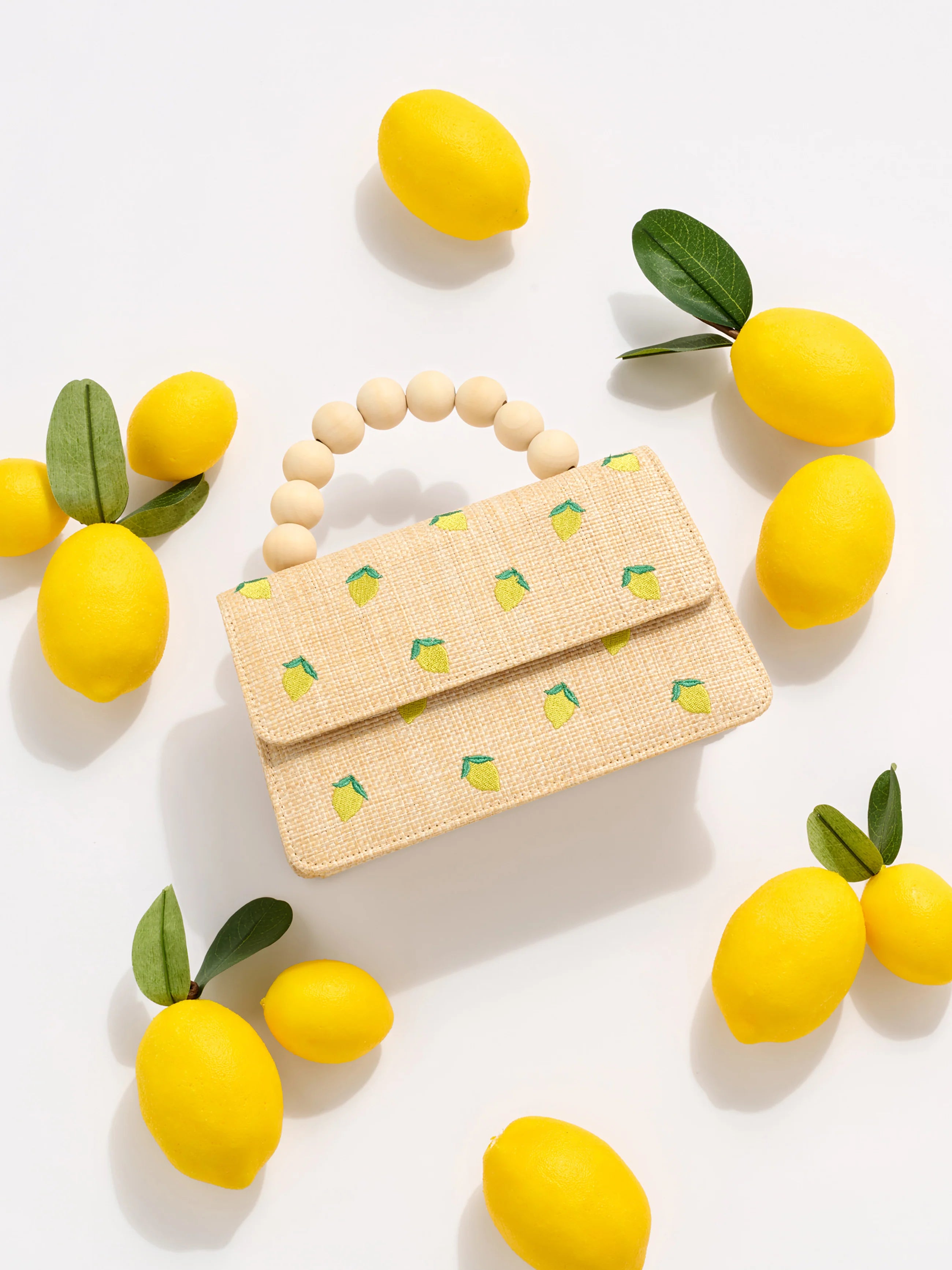 Small woven handbag with lemon pattern surrounded by lemons on a white background