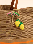 Brown textured bag with a pink umbrella and yellow lemon charm on a beige background