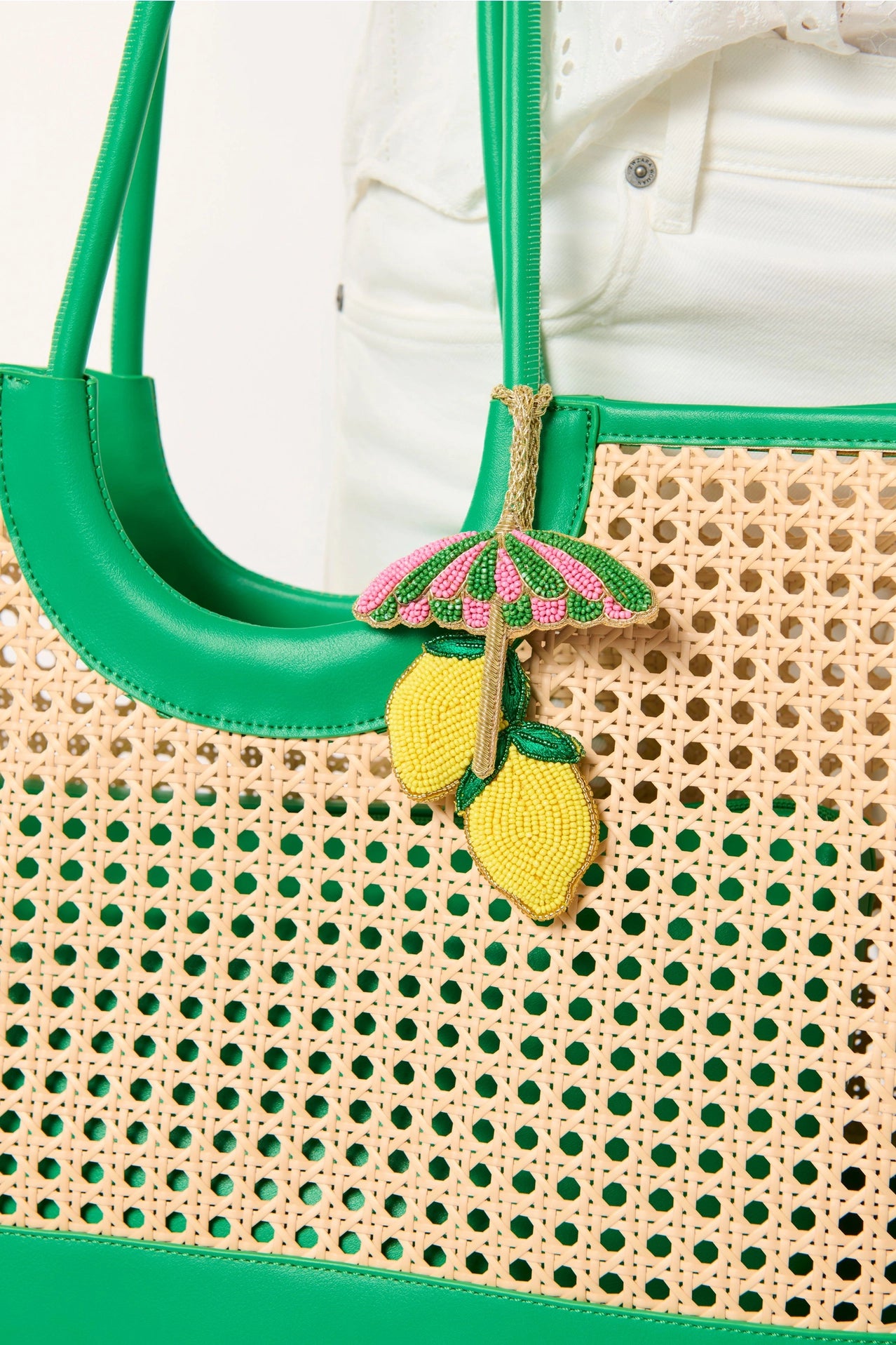 Beige woven handbag with green accents and decorative lemon and umbrella charm.
