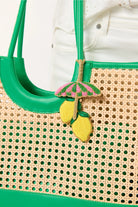Beige woven handbag with green accents and decorative lemon and umbrella charm.