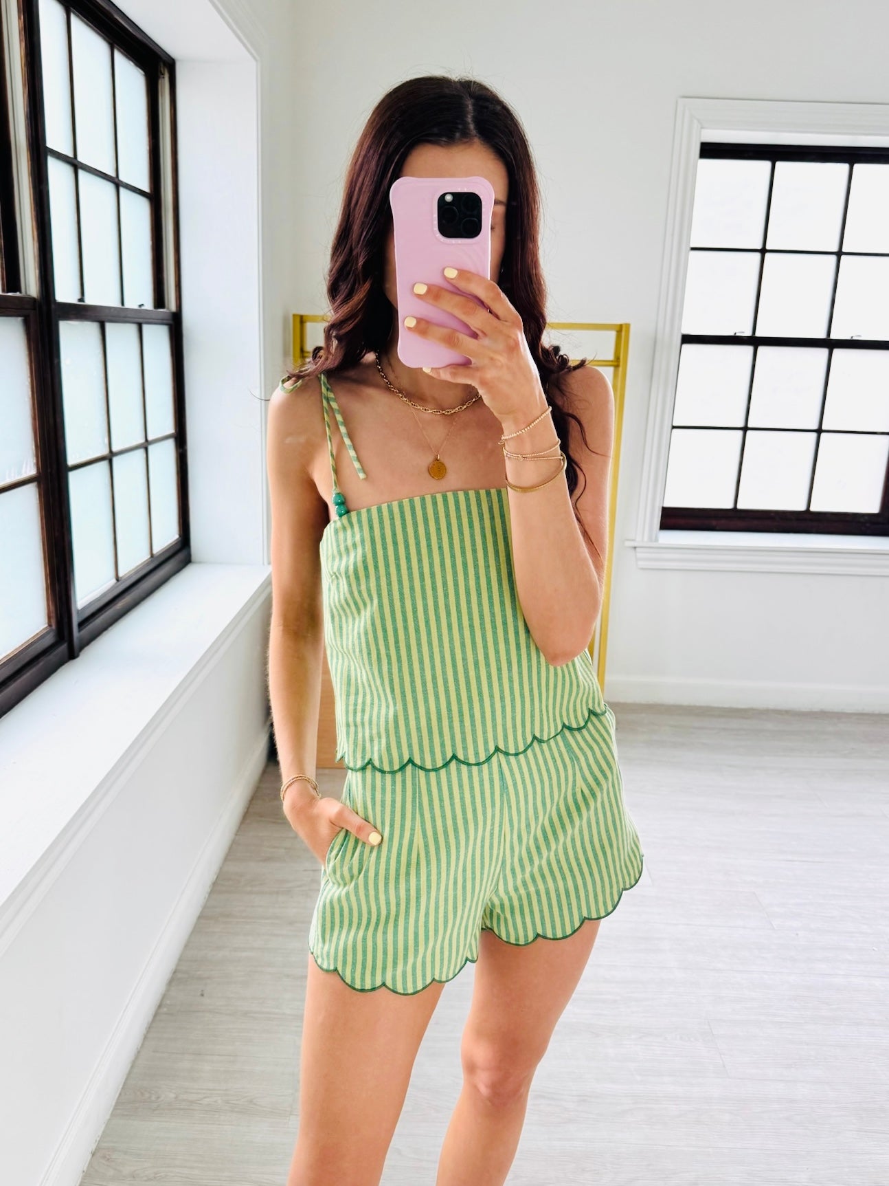 Woman taking a mirror selfie wearing a green and white striped dress in a bright room.