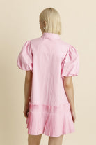 Person wearing a pink dress with puffed sleeves on a beige background