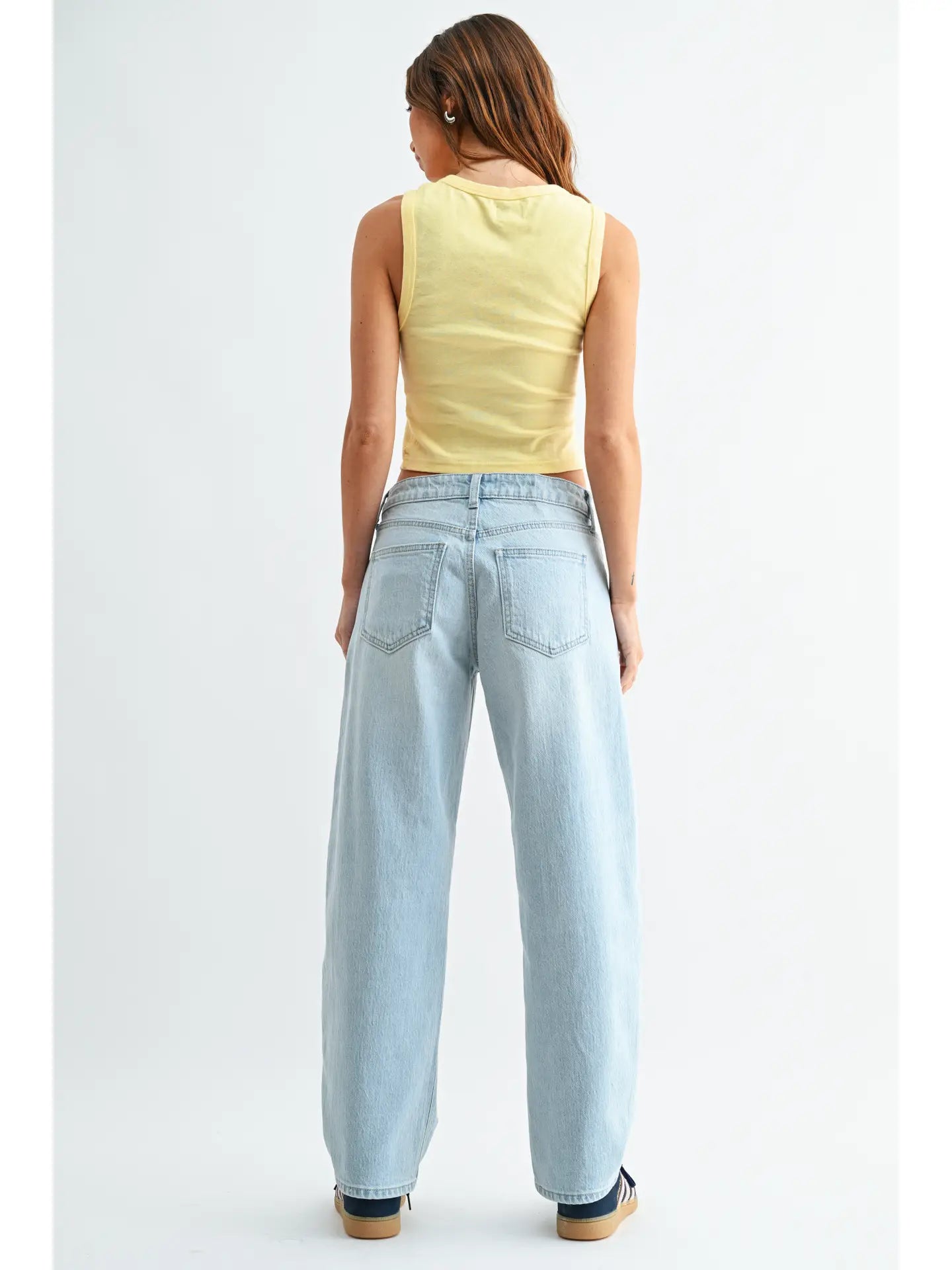 Woman wearing light blue jeans and a yellow sleeveless top on a white background
