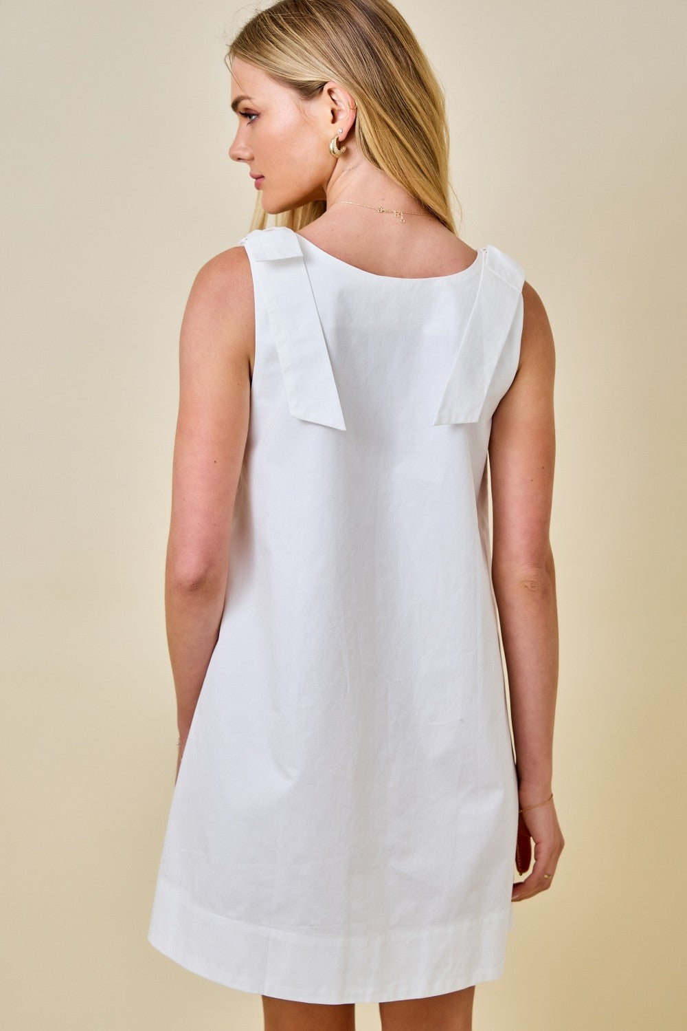 Woman wearing a white dress with ruffled shoulders against a beige background