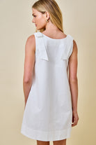 Woman wearing a white dress with ruffled shoulders against a beige background