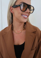 Woman wearing sunglasses and a brown coat with a white background