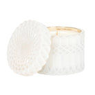 A white textured glass jar candle with its lid leaning against it, set against a clean white background.