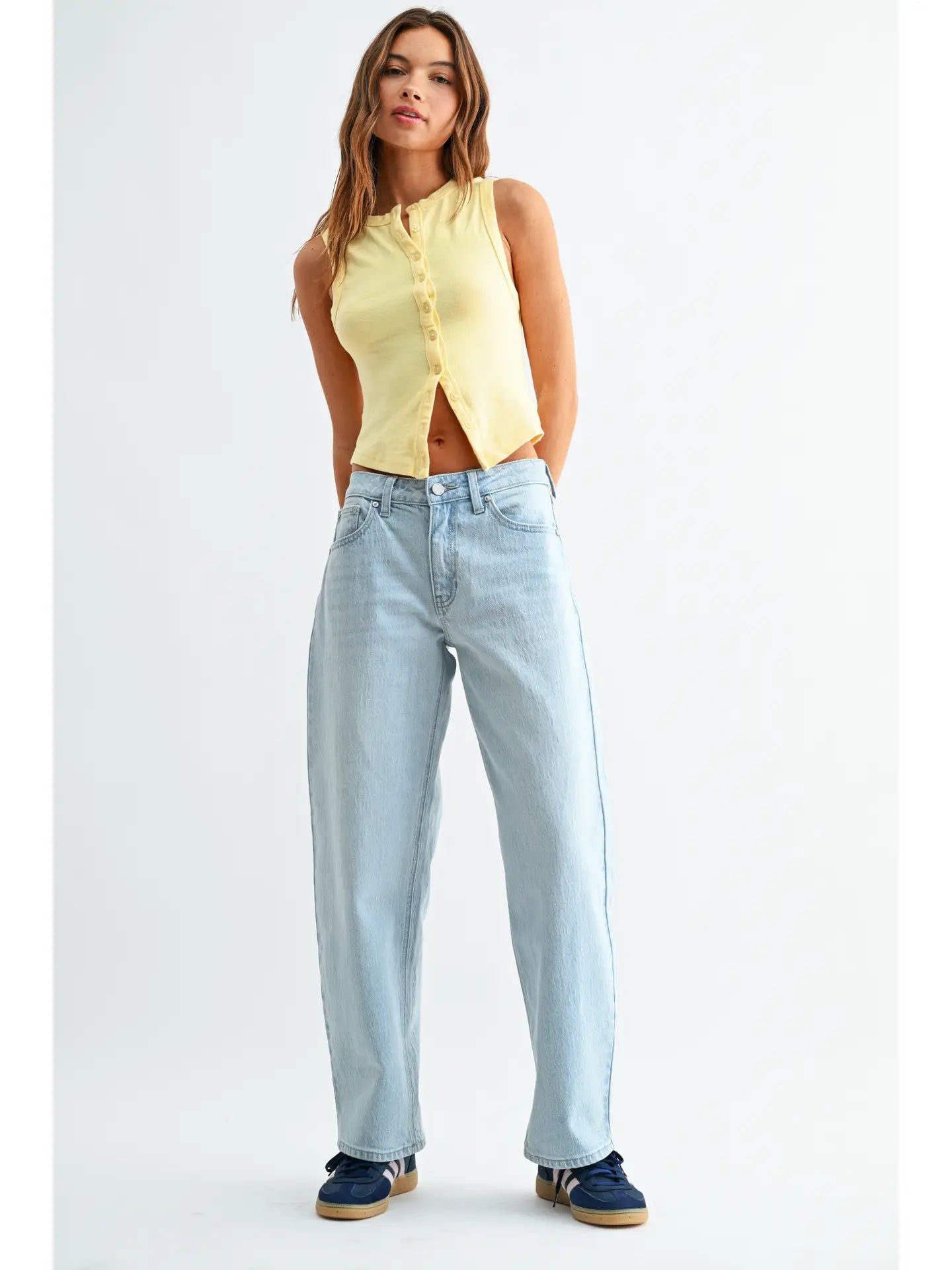 Woman wearing a yellow sleeveless top and light blue jeans on a white background