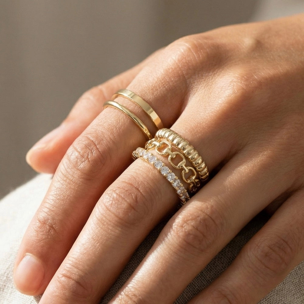 Close-up of a hand wearing multiple gold rings with a neutral background