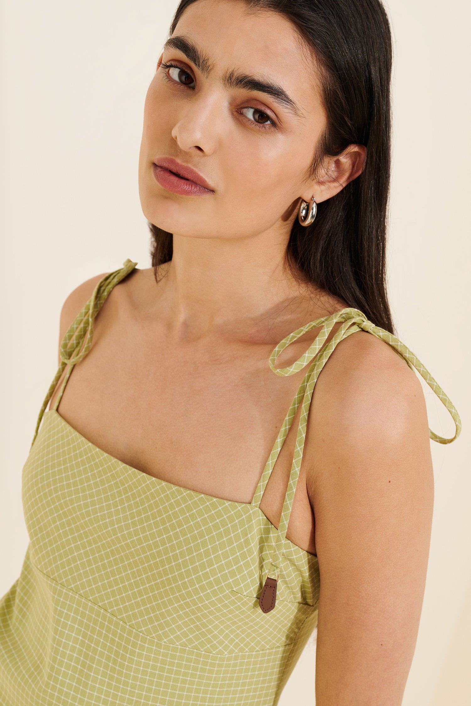 Woman wearing a green dress with tied straps on a beige background