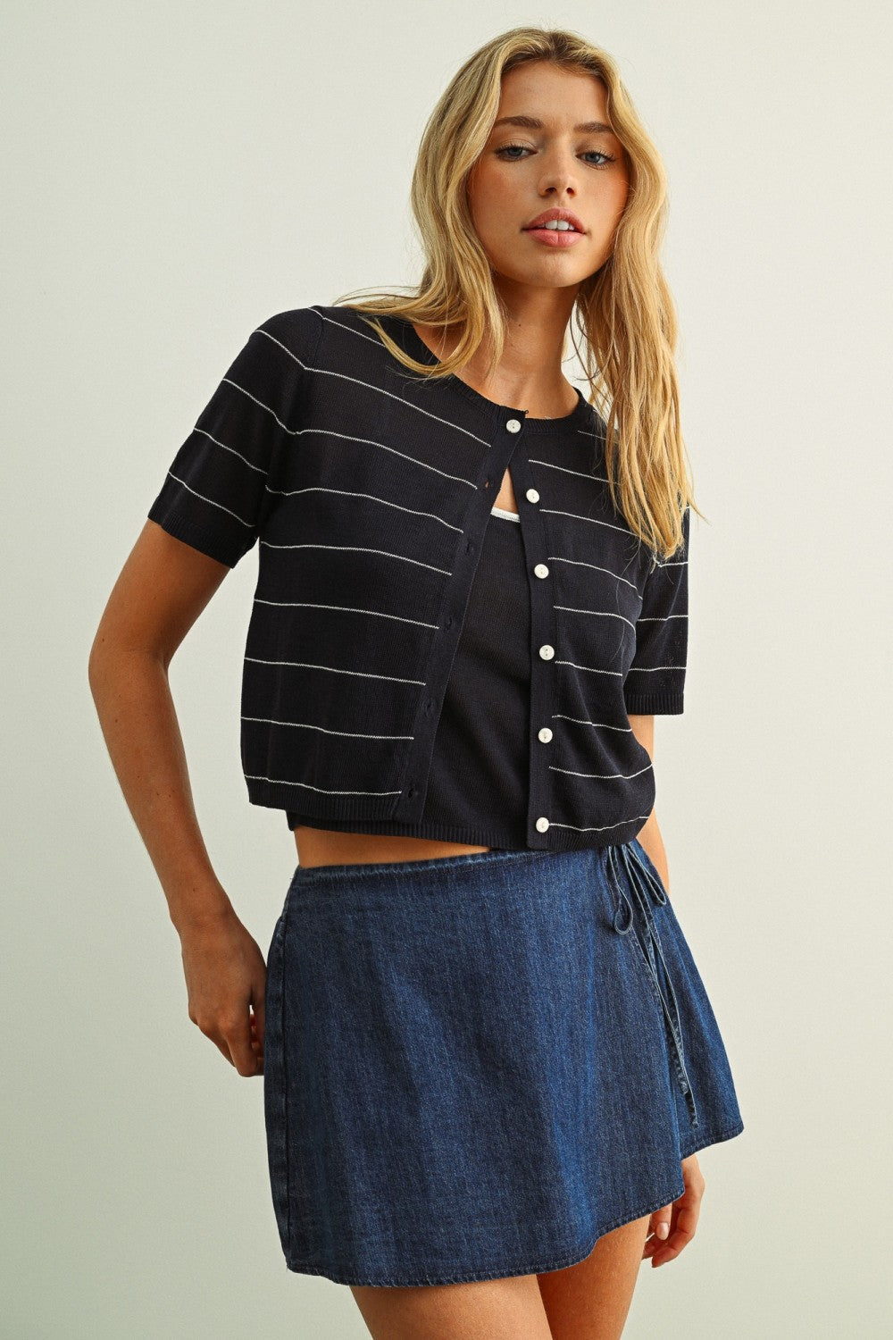 Woman wearing a black striped shirt and blue denim skirt on a plain background