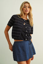 Woman wearing a black striped shirt and blue denim skirt on a plain background