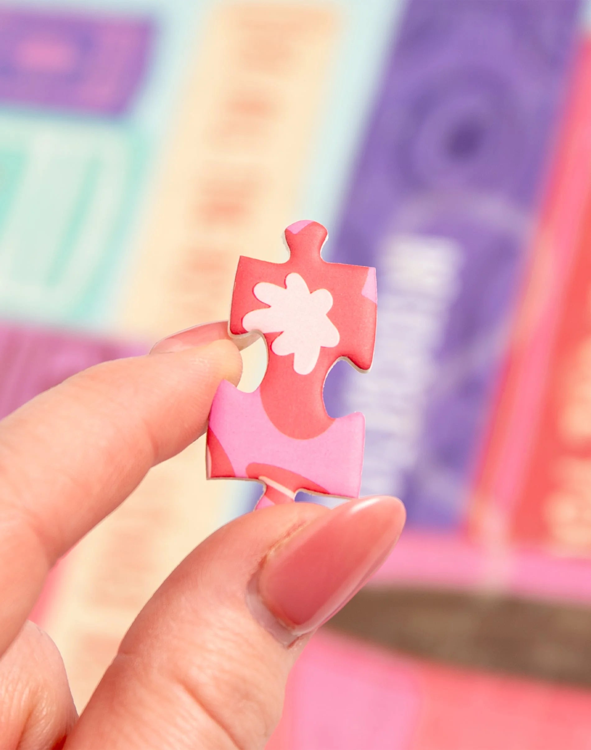Pink puzzle piece with a white flower design held by a hand against a colorful background