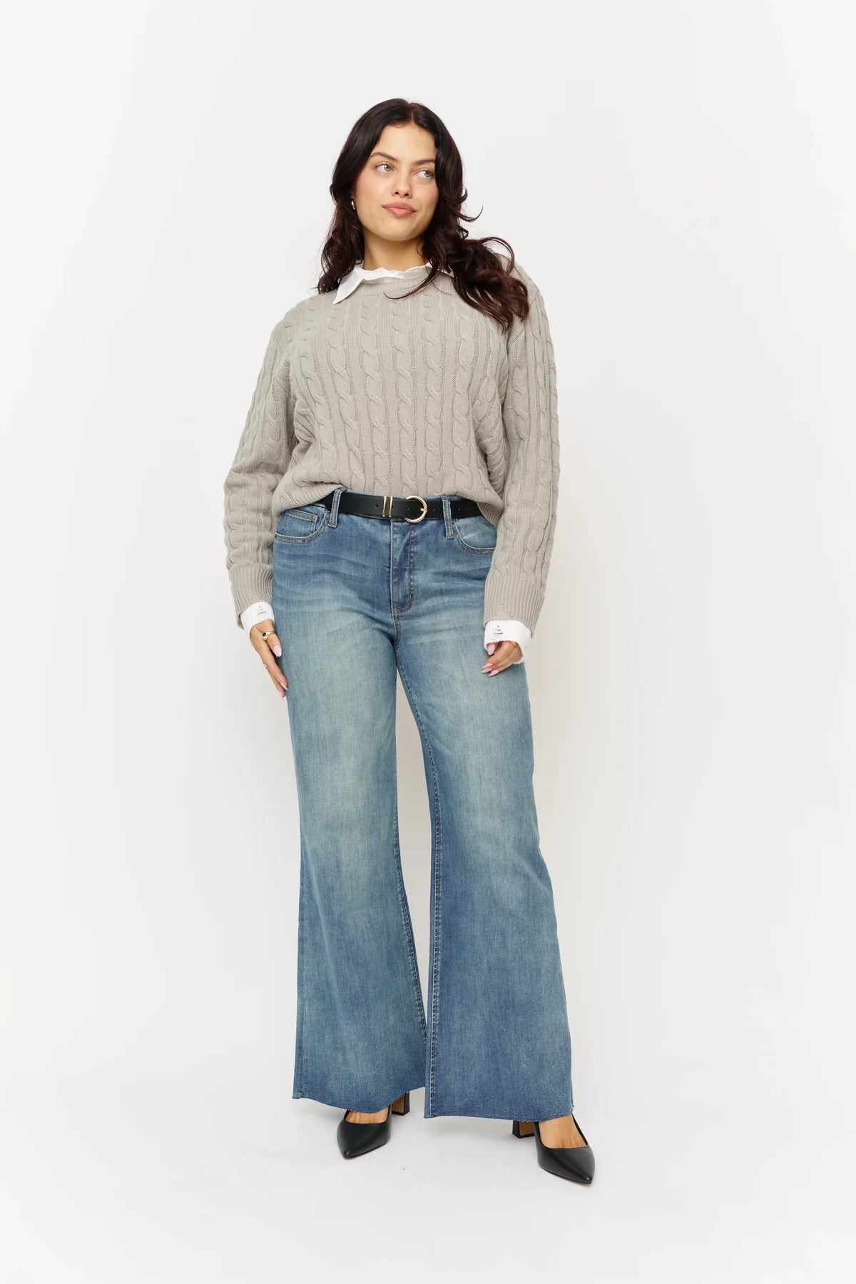 Woman wearing a beige sweater and blue jeans on a white background