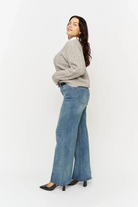 Woman wearing a gray sweater and blue jeans on a white background