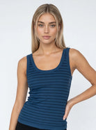 A woman modeling a sleeveless scoop-neck tank top with horizontal dark blue and navy stripes, paired with black bottoms, against a light gray studio background. 