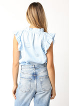 Woman wearing a light blue ruffled top and jeans on a white background