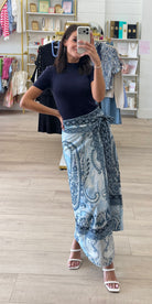 A woman takes a mirror selfie in a boutique while wearing a navy blue short-sleeve top and a long, flowing blue paisley wrap skirt with white straps.