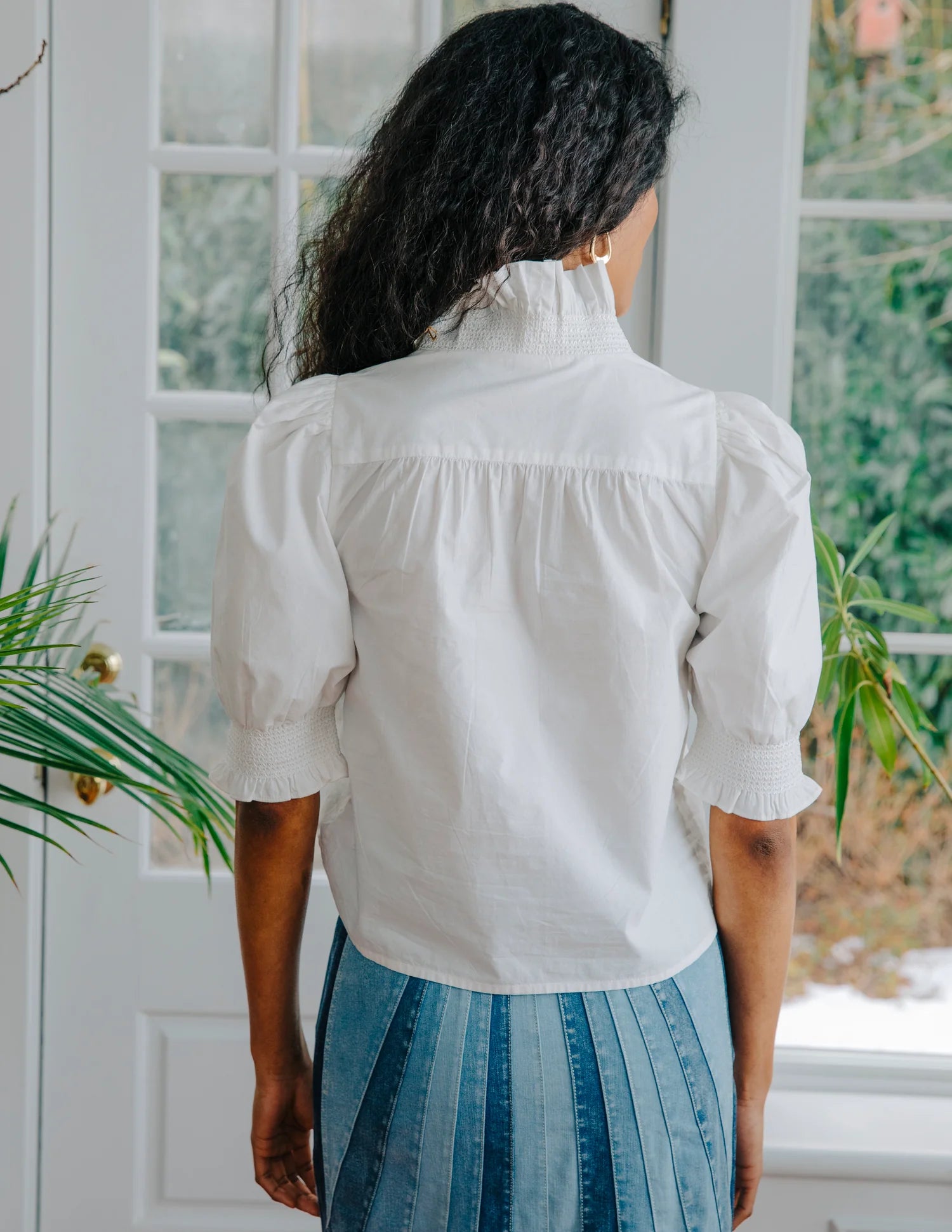 Person wearing a white blouse with puffed sleeves in a room with plants.