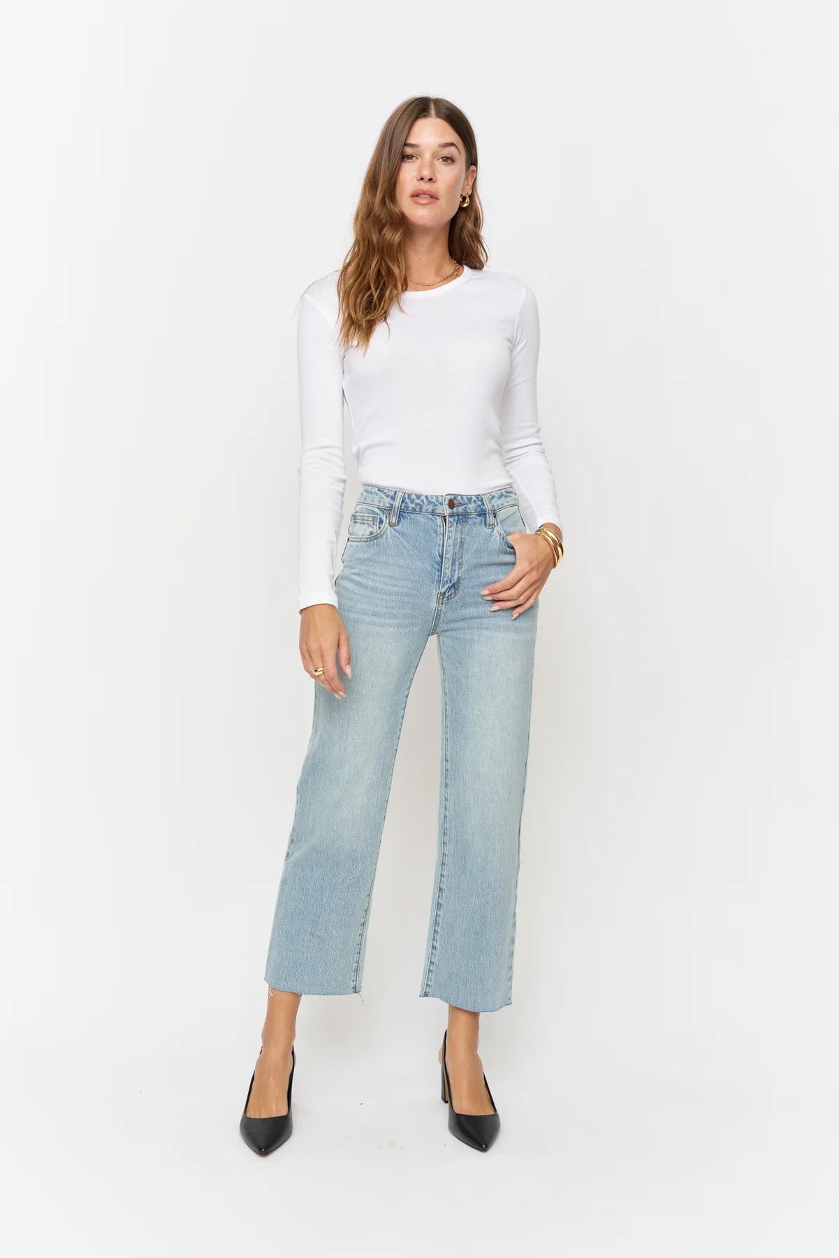 Woman wearing a white long-sleeve top and light blue jeans on a white background
