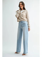 A woman modeling a light beige cropped cardigan over a white top and light blue wide-leg jeans, standing against a plain light gray studio background.