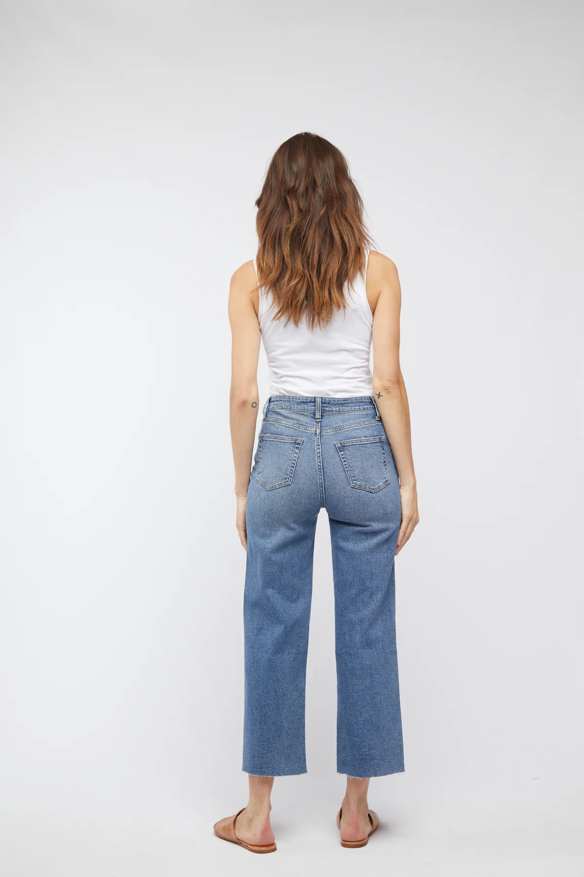 Person wearing light blue jeans and a white tank top on a plain background