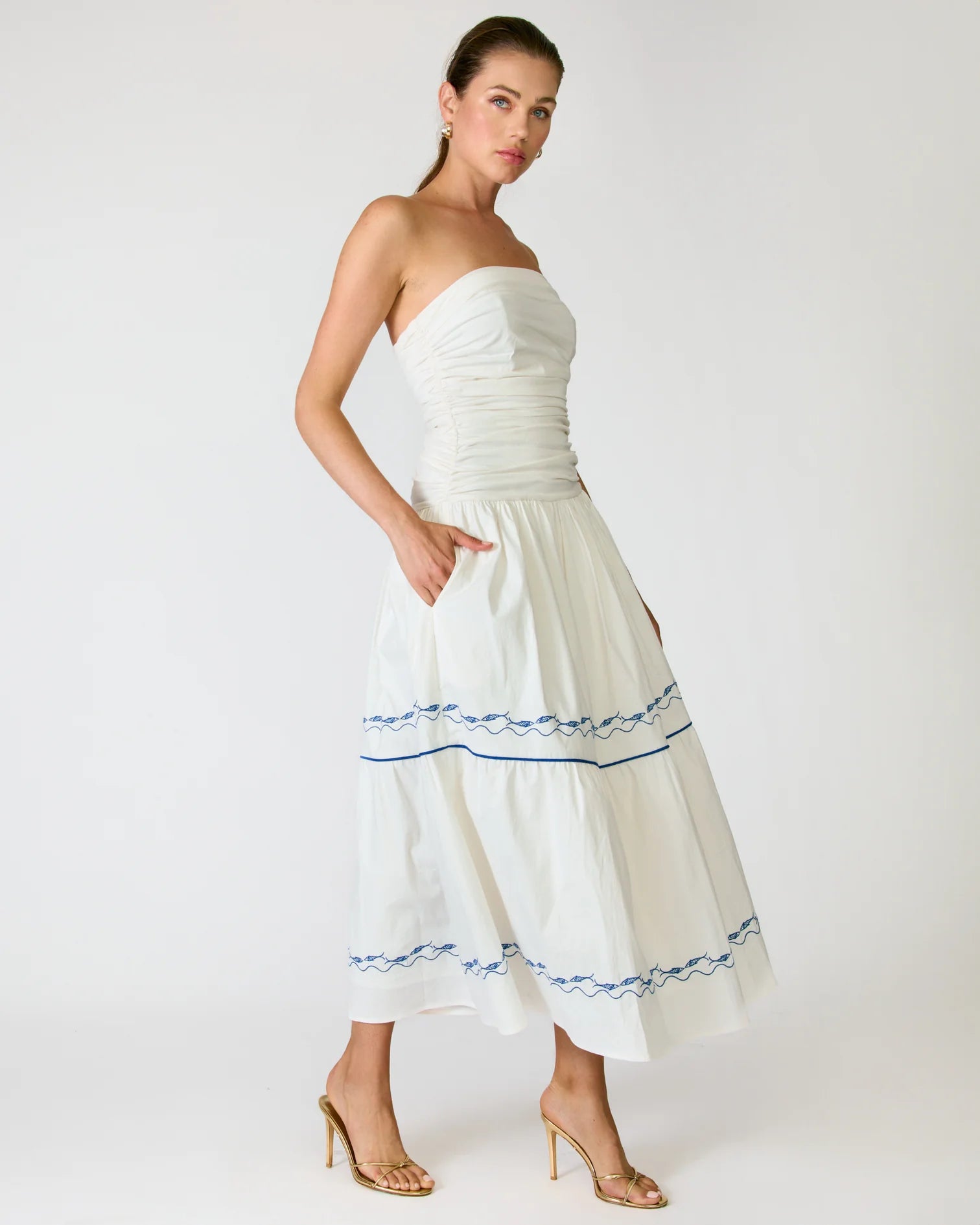 Woman wearing a white strapless dress with blue trim on a white background