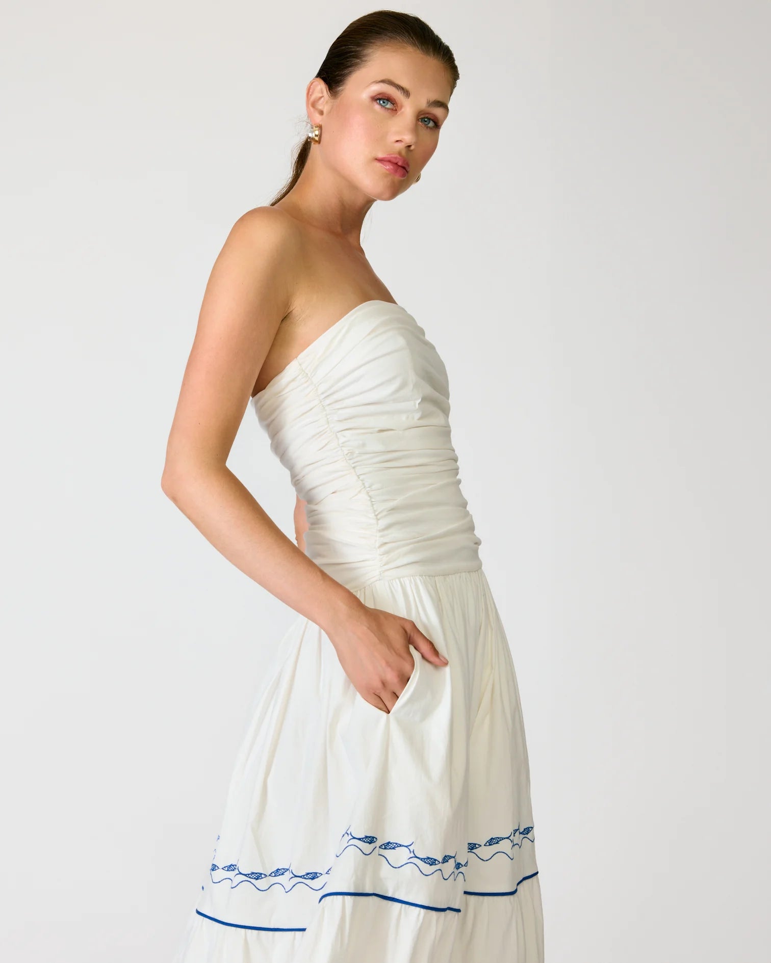 Woman wearing a white strapless dress with blue embroidery on a plain background
