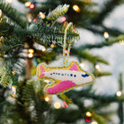 Colorful airplane needlepoint ornament on a Christmas tree with blurred lights in the background