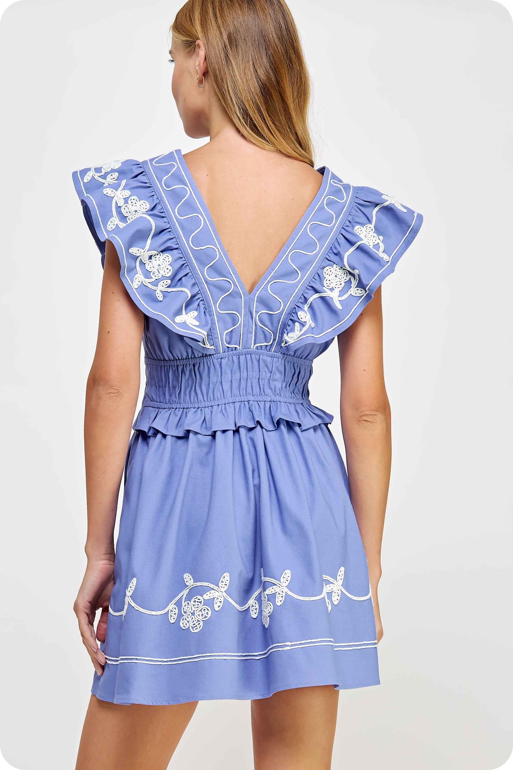 Woman wearing a blue dress with white embroidery on a light gray background