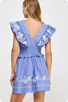 Woman wearing a blue dress with white embroidery on a light gray background