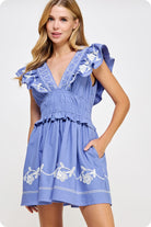 Woman wearing a blue dress with white embroidery on a white background