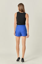 Woman wearing a black sleeveless top and blue shorts on a plain background