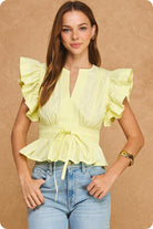 Woman wearing a yellow blouse with ruffled sleeves and blue jeans on a beige background