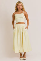 Woman wearing a light yellow top and skirt set against a plain background