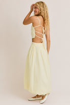 Woman wearing a light yellow dress with a strappy back on a plain background