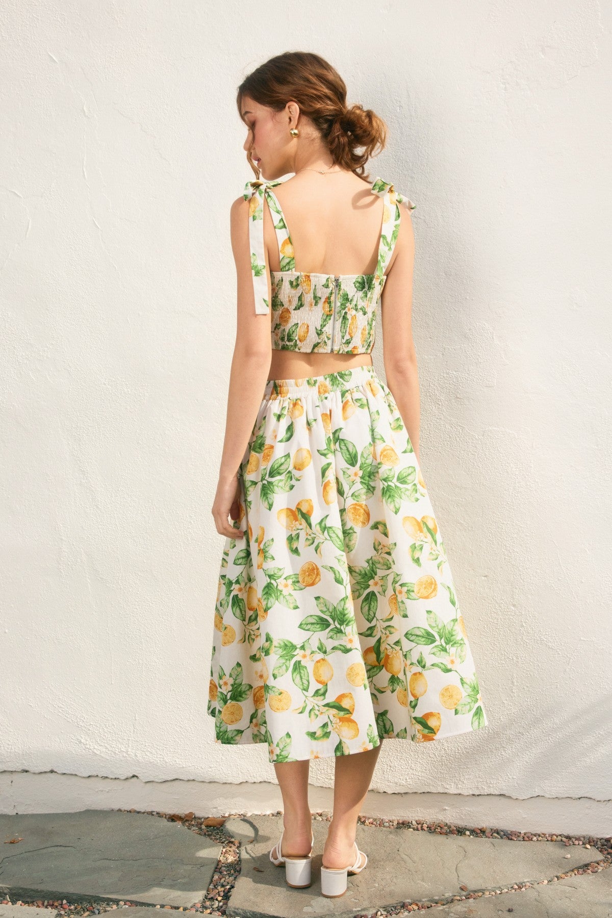 Woman wearing a floral dress with lemon pattern against a white wall.