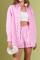 Woman wearing a pink eyelet cover-up with a white top and shorts on a green background