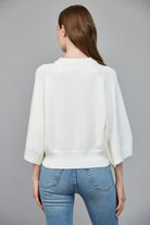 Person wearing a white sweater and blue jeans on a gray background