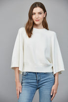Woman wearing a white blouse and blue jeans against a gray background