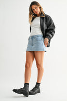 Woman wearing a black jacket, white shirt, denim skirt, and black boots on a white background