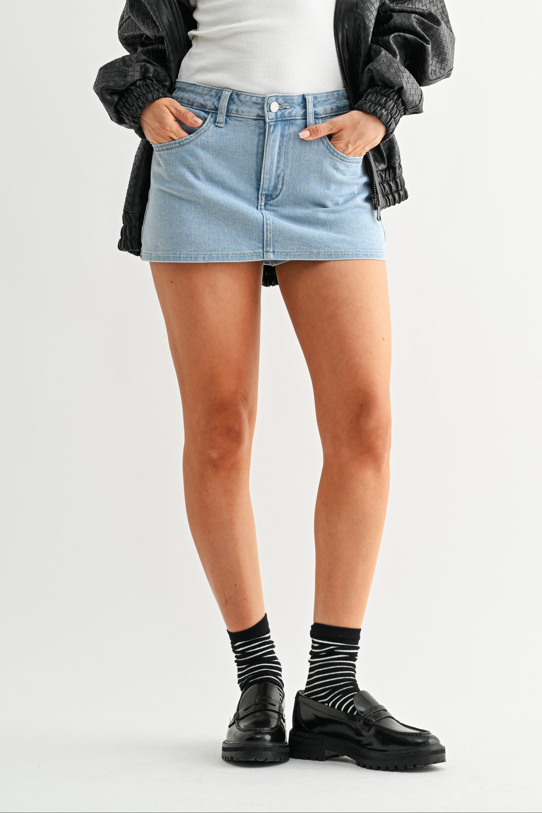 Woman wearing a white tank top, denim skirt, black jacket, and black shoes on a white background