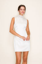 Woman wearing a white sleeveless dress against a plain background
