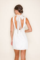 Woman wearing a white dress with a bow detail on the back against a beige background