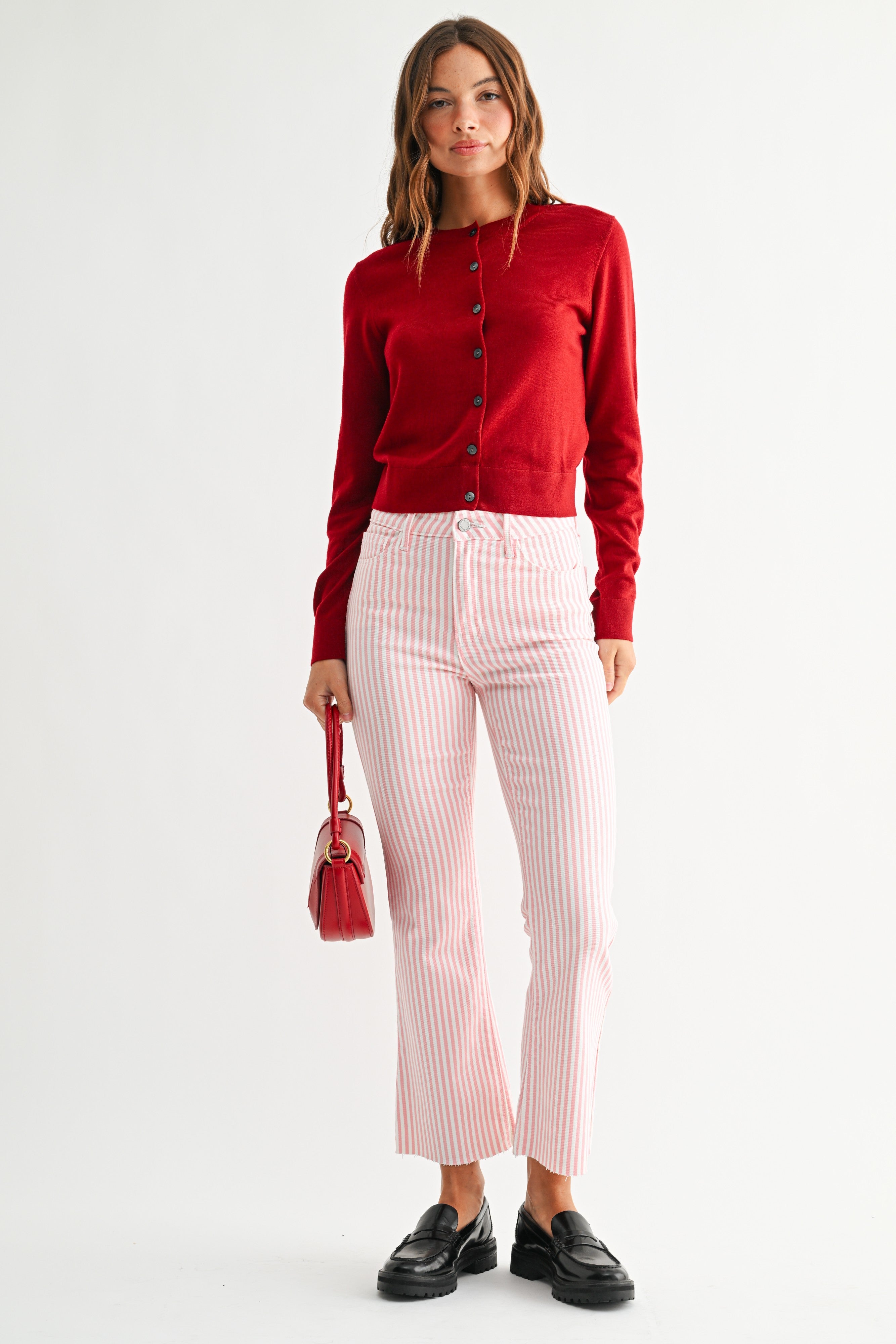 Woman wearing a red cardigan, pink striped pants, and black shoes on a white background